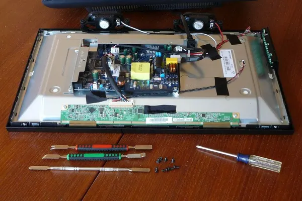 Small LCD TV opened on a table, with its boards exposed and tools beside it